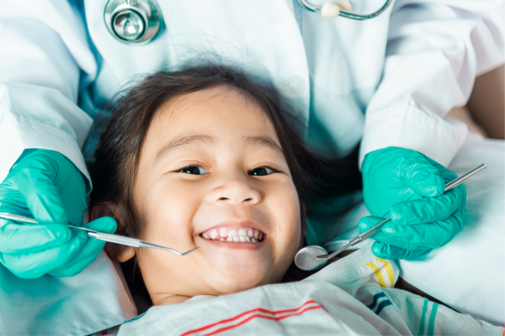 A young child smiling broadly while being examined by a dentist