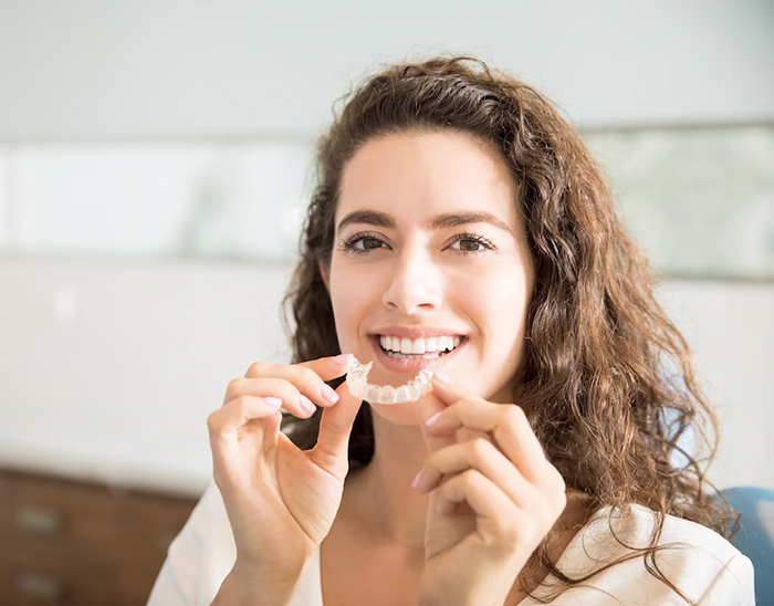 A woman holding her aligner in front of her open mouth